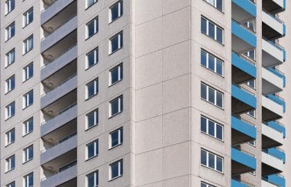 Nahaufnahme der Gebäudeecke eines Hochhauses mit Betonfassade, schmalen Fensterbändern und Balkonen mit blauen Brüstungen.