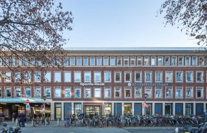 Viergeschossiges Backsteingebäude mit Bankfiliale im Erdgeschoss, davor Hunderte abgestellter Fahrräder und herbstliches Laub.