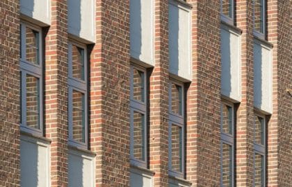 Fassadendetail: Backsteinwand mit senkrechten Fensterreihen und hellen Putzfeldern zwischen den Geschossen.