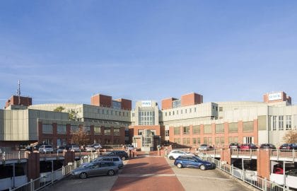 Weitläufiger Bürokomplex aus Backstein und hellen Metallpaneelen mit vorgelagerten Parkdecks und gepflasterter Zufahrt.