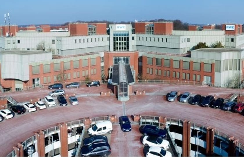 Luftaufnahme eines symmetrischen Bürokomplexes mit verglastem Mittelbau und zwei halbrund vorgelagerten Parkdecks.