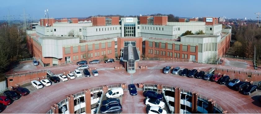 Luftaufnahme eines symmetrischen Bürokomplexes mit verglastem Mittelbau und zwei halbrund vorgelagerten Parkdecks.