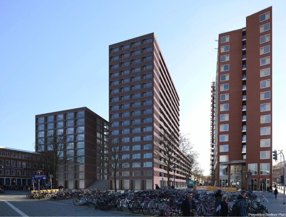 Architekturvisualisierung mit zwei rotbraunen Neubaukörpern unterschiedlicher Höhe über einem Vorplatz mit dichter Fahrradabstellanlage.