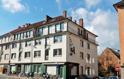 Verputztes Eckwohnhaus mit Mansarddach, Balkonen und einem figürlichen Wandrelief, im Erdgeschoss grün gefasste Ladenfronten.