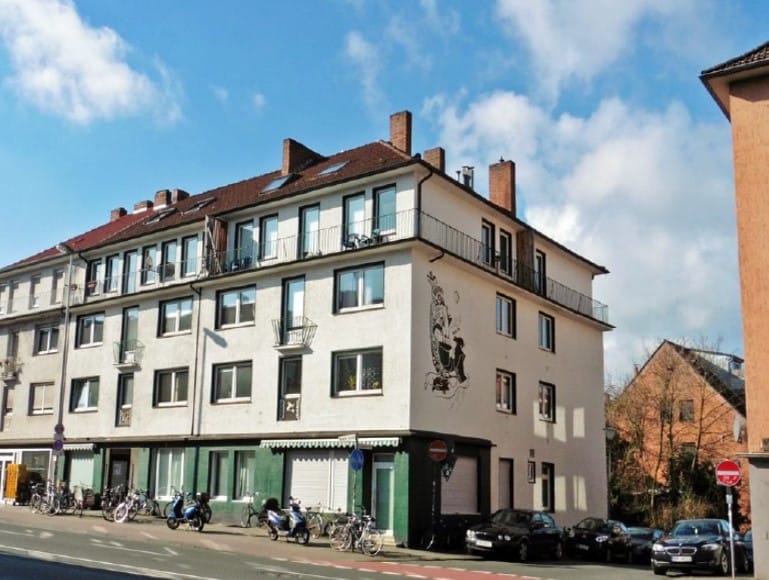 Verputztes Eckwohnhaus mit Mansarddach, Balkonen und einem figürlichen Wandrelief, im Erdgeschoss grün gefasste Ladenfronten.
